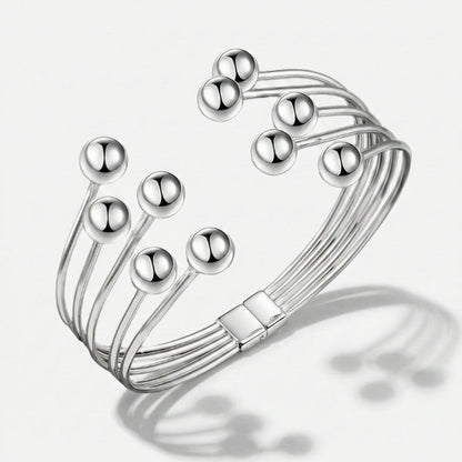 Damenarmband mit mehreren glatten Metallreihen und polierten Kugelenden, in Gold- oder Silberoptik am Handgelenk und in Detailansicht dargestellt